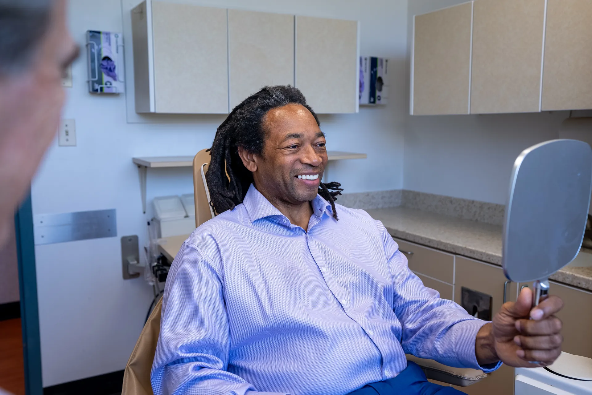 A patient smiling while holding a hand mirror in the treatment chair at Elite Prosthetic Dentistry
