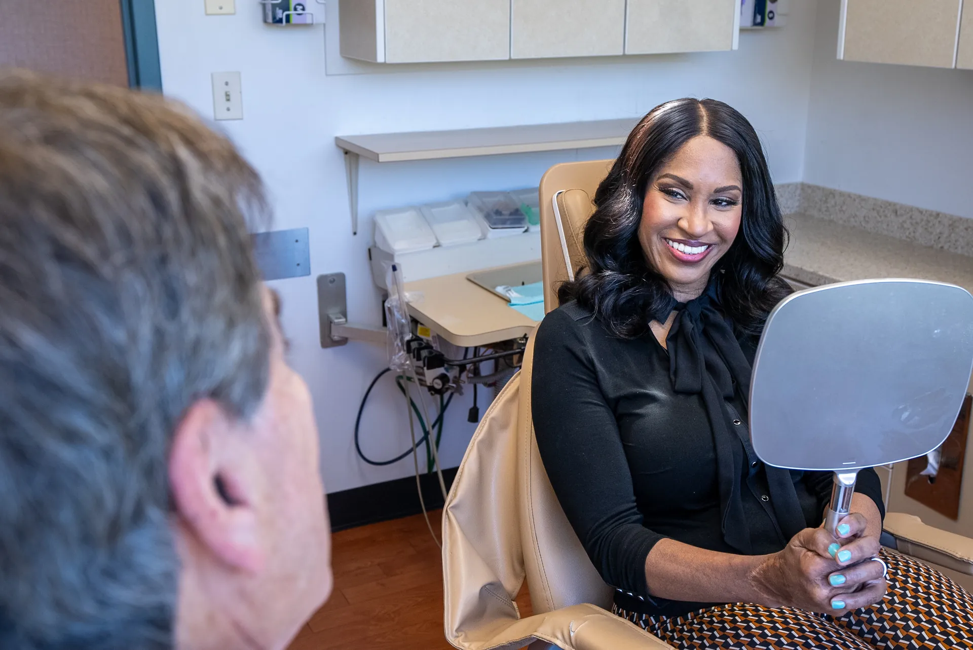 A patient viewing her smile in a hand mirror in the treatment chair at Elite Prosthetic Dentistry